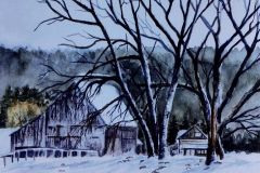 An old barn and farmhouse behind leaveless trees in winter.