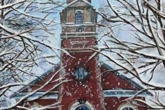 A red church in the snow seen through some snowy bare tree branches.